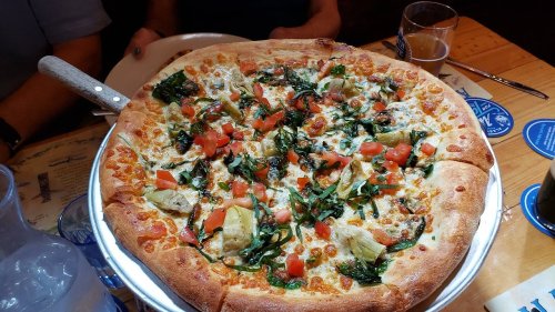 A large pizza topped with spinach, artichokes, tomatoes, and melted cheese, served on a wooden table.
