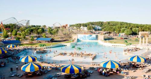 A vibrant water park scene with a wave pool, colorful umbrellas, and people enjoying the sun and water attractions.