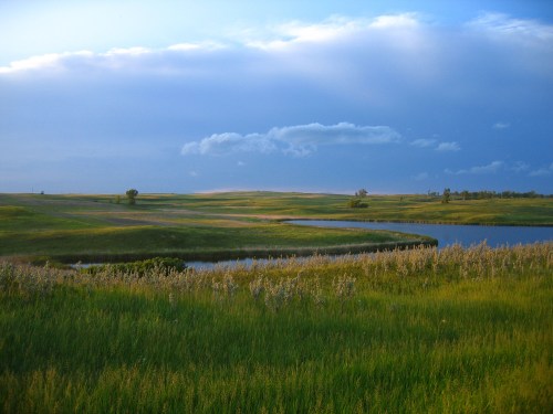 A serene landscape featuring rolling green hills, a winding river, and a blue sky with scattered clouds.