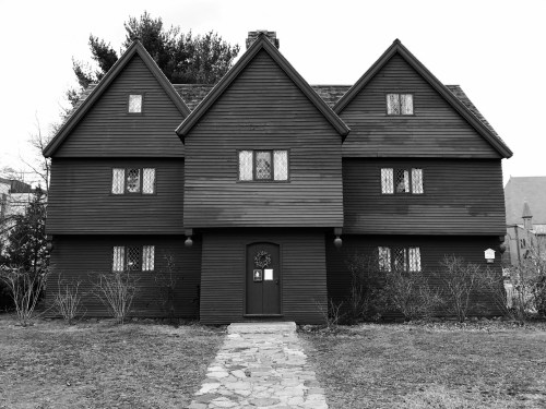 A large, dark wooden house with a unique triangular roof and stone pathway, surrounded by bare shrubs.