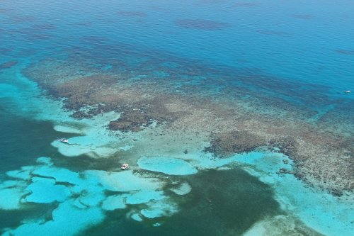 Aerial view of vibrant turquoise waters and coral reefs, with small boats scattered across the serene ocean surface.