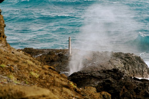 A rocky coastline with ocean waves and steam rising from a vent, creating a misty atmosphere.