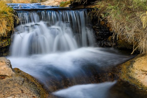 A serene waterfall cascading over rocks, surrounded by grass and natural scenery.