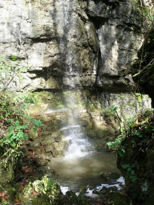 A serene waterfall cascading over rocky terrain, surrounded by lush greenery and natural stone.