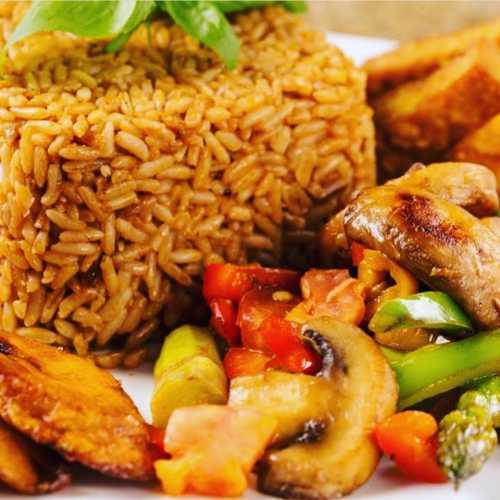 A plate of rice, fried plantains, grilled vegetables, and mushrooms, garnished with fresh herbs.