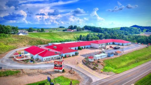 Aerial view of a large building with a red roof, surrounded by green hills and a clear blue sky.
