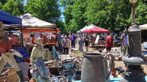 A bustling outdoor market with various tents, people browsing, and vintage items displayed in the foreground.