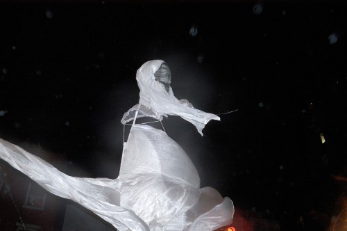 A ghostly figure draped in white fabric stands against a dark night sky, creating an eerie atmosphere.