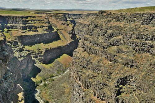 A vast canyon with steep, rocky cliffs and a winding river at the bottom, surrounded by green vegetation.
