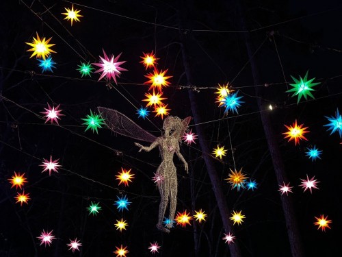 A whimsical fairy figure surrounded by colorful star-shaped lights against a dark night sky.