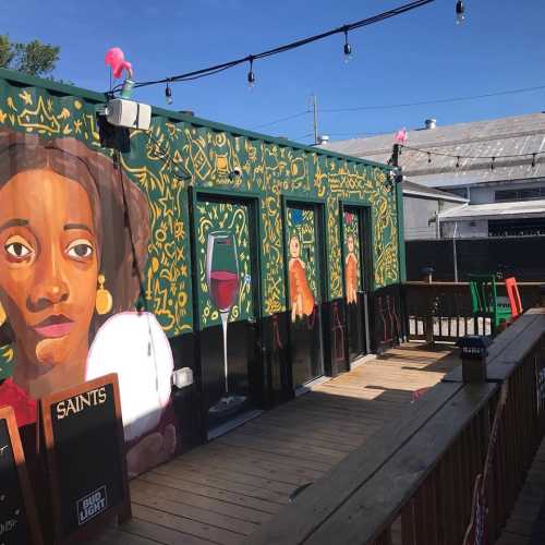 A vibrant mural of a woman adorns a colorful outdoor space with string lights and wooden decking.