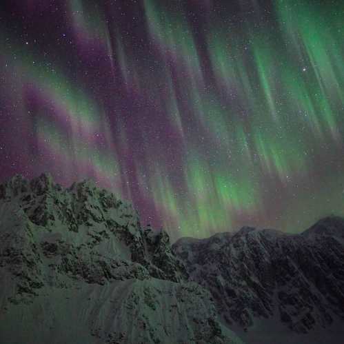 A stunning display of the northern lights over snow-capped mountains, with vibrant green and purple hues in the sky.
