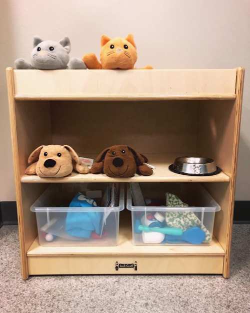 A wooden toy shelf with stuffed animals on top and two bins below, containing various toys and a dog bowl.