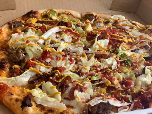 A pizza topped with lettuce, salsa, mustard, and ground meat, served in a cardboard box.
