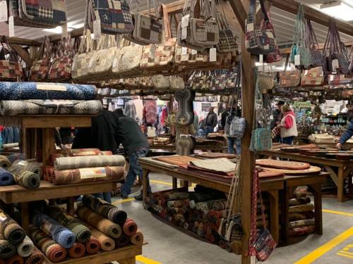 A bustling market with shelves of colorful fabrics and bags, surrounded by shoppers exploring the vibrant displays.