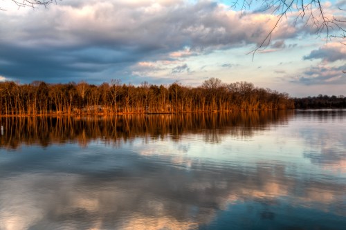 A serene lake reflecting trees and clouds at sunset, with warm colors illuminating the water's surface.