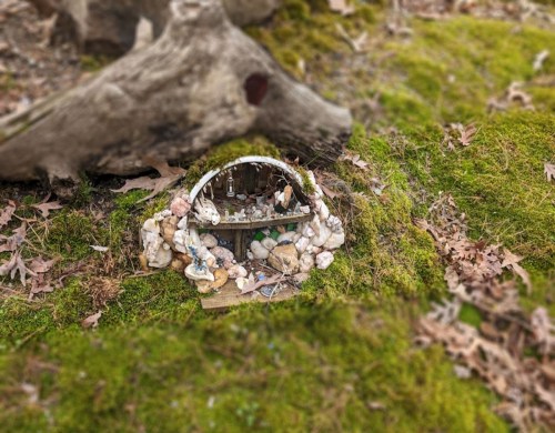 A whimsical miniature house surrounded by stones and moss, nestled in a forest setting.