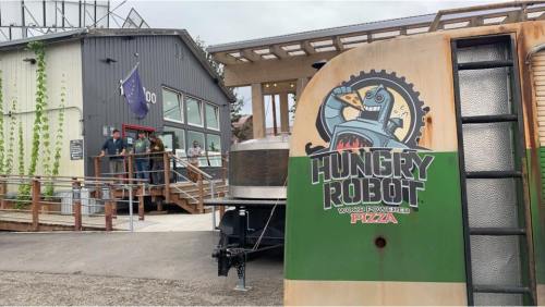 A food truck with a "Hungry Robot" logo parked outside a modern building, with people entering and a flag flying.