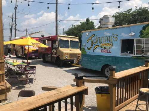 A vibrant food truck area featuring colorful trucks and outdoor seating under string lights on a sunny day.