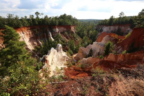 A scenic view of colorful canyon walls with trees and a cloudy sky in the background.
