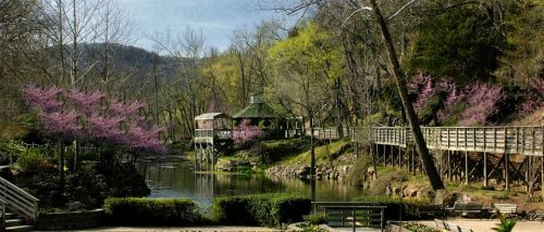 A serene park scene featuring a gazebo by a calm lake, surrounded by blooming trees and lush greenery.