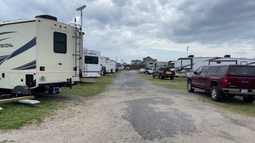 A gravel road lined with RVs and trucks under a cloudy sky, leading to a distant building.