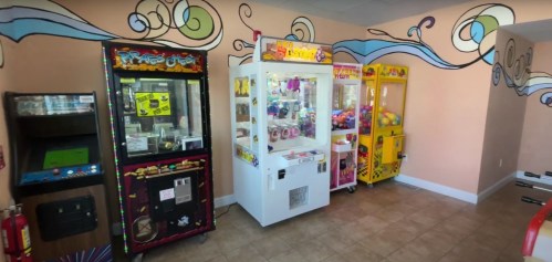 A colorful arcade featuring claw machines and a game cabinet against a muraled wall.