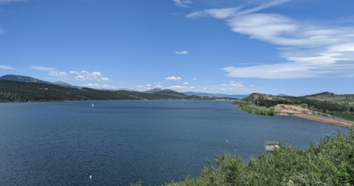 A serene lake surrounded by mountains under a blue sky with scattered clouds.