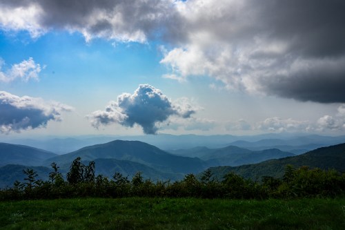 A scenic view of mountains under a partly cloudy sky, with lush greenery in the foreground and distant peaks.