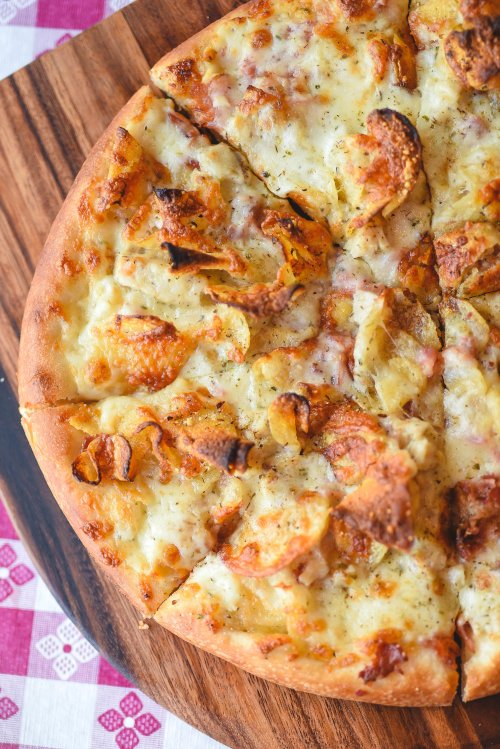 A freshly baked pizza topped with melted cheese and crispy potato slices, served on a wooden board.