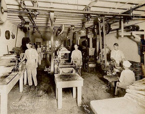 Historic printing workshop with workers operating machinery and printing presses in a spacious industrial setting.