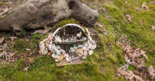 A small, whimsical fairy house made of stones and natural materials, nestled in moss and leaves on the forest floor.