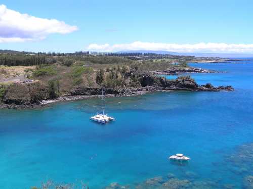 A serene coastal view featuring a turquoise bay with sailboats and lush green hills in the background.