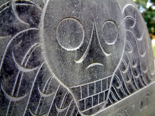 Close-up of a weathered gravestone featuring a skull design with intricate swirling patterns.