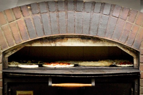 A brick oven with several pizzas baking inside on a metal tray.