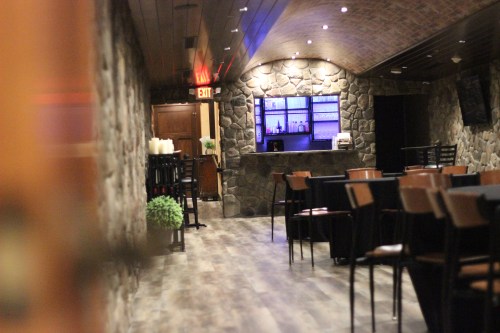 Interior of a dimly lit restaurant with stone walls, a bar area, and tables set for dining.