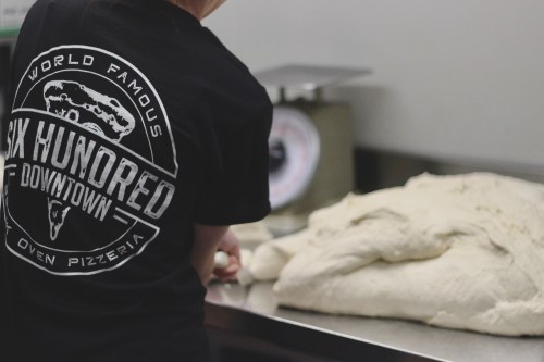 A person in a black shirt prepares pizza dough on a countertop at a pizzeria.