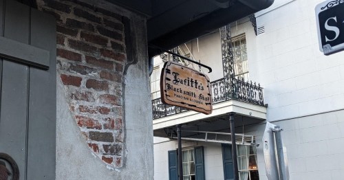 Sign for "Jazzy's Blacksmith Shop" hangs above a brick wall, with a balcony visible in the background.