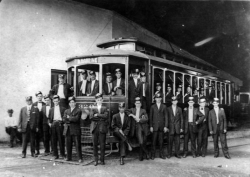 A historic black-and-white photo of a group of men, including trolley operators, posing in front of a streetcar.