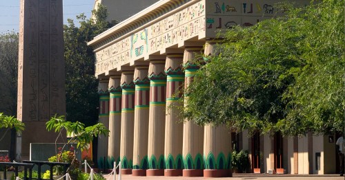 Ancient-style building with columns, hieroglyphs, and lush greenery in the foreground.