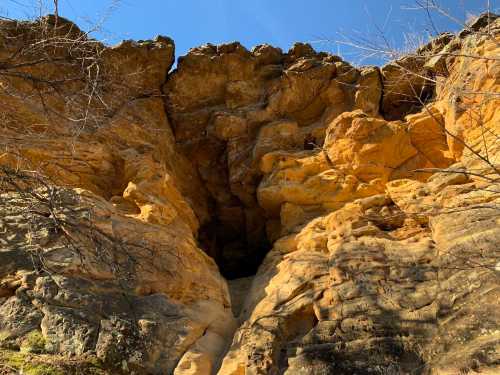 A rocky cliff with orange and brown hues, featuring a narrow opening at the top against a clear blue sky.