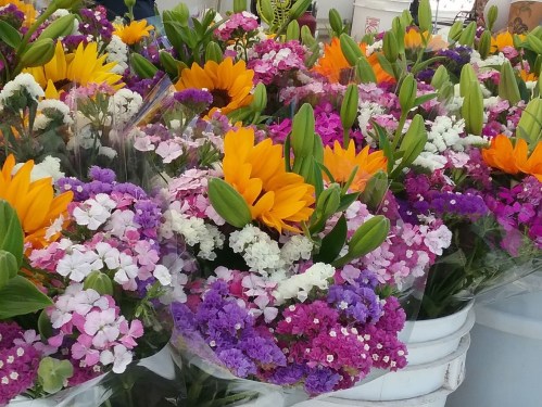 A vibrant display of colorful flowers, including sunflowers, lilies, and various blooms in shades of purple and pink.