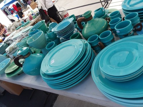 A variety of turquoise ceramic dishes, including plates, bowls, and mugs, displayed on a table at a market.