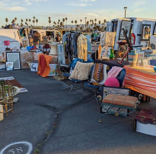 A vibrant outdoor market scene with various vintage items, clothing, and furniture displayed on a sunny day.