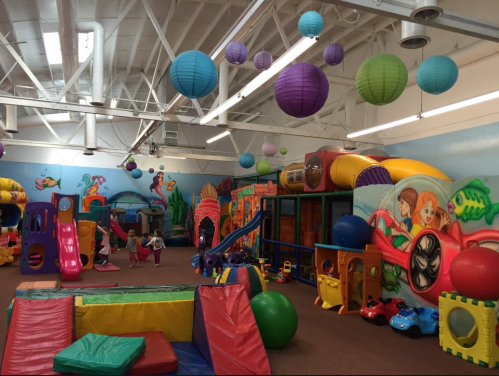 Colorful indoor play area with various climbing structures, slides, and soft play equipment, decorated with hanging lanterns.