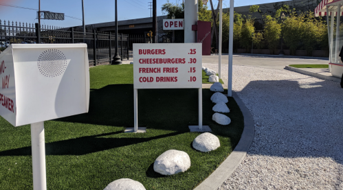 A menu board displays prices for burgers, cheeseburgers, French fries, and cold drinks outside a restaurant.