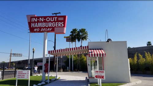 In-N-Out Burger restaurant with a red and white sign, palm trees, and a clear blue sky.