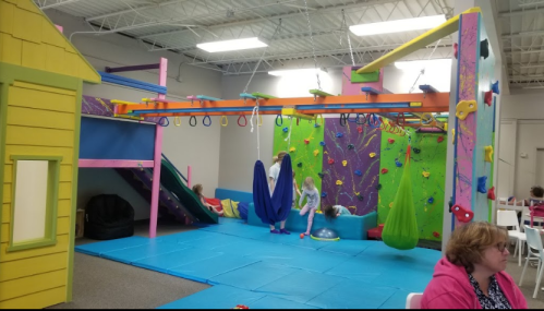 Colorful indoor play area with climbing walls, swings, and slides, featuring children playing and exploring.