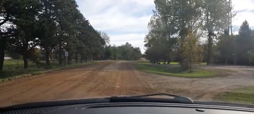 A view from a car dashboard on a dirt road surrounded by trees and greenery, with a fork in the road ahead.