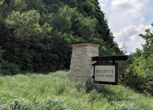 Sign for Bellevue State Park surrounded by lush greenery and trees under a partly cloudy sky.